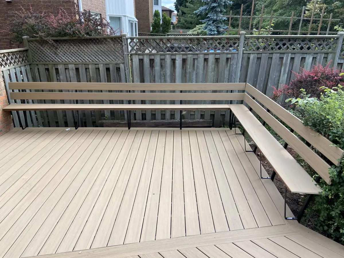 A light grey-brown composite deck with an L-shaped built-in bench with a backrest running along a lattice-topped fence.