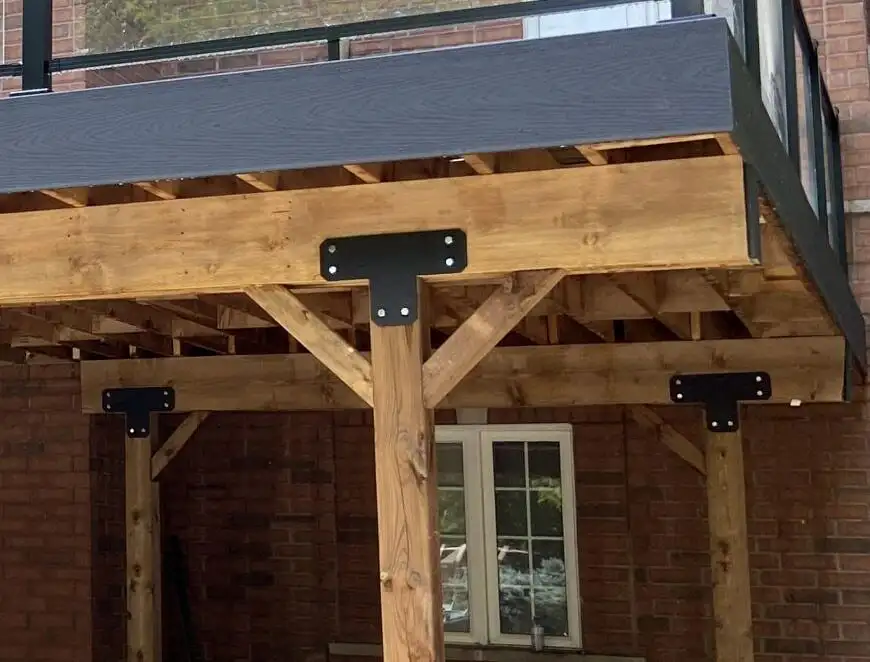 Underneath one of Evenstar's raised decks: a charcoal composite fascia, joist ends, a timber beam, a timber post fixed to it with a black steel bracket, and two angled knee braces.