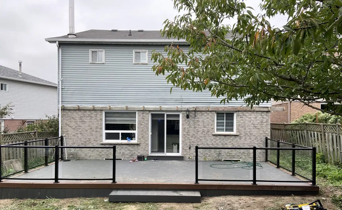 A low grey composite deck with black aluminum railings across the back of a house with blue siding and a brick base.