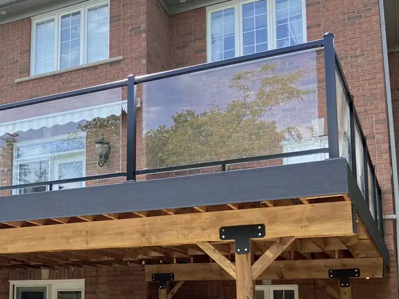 A raised Evenstar deck with glass railing on a red-brick house, carried on timber posts with angled knee braces and black steel brackets.