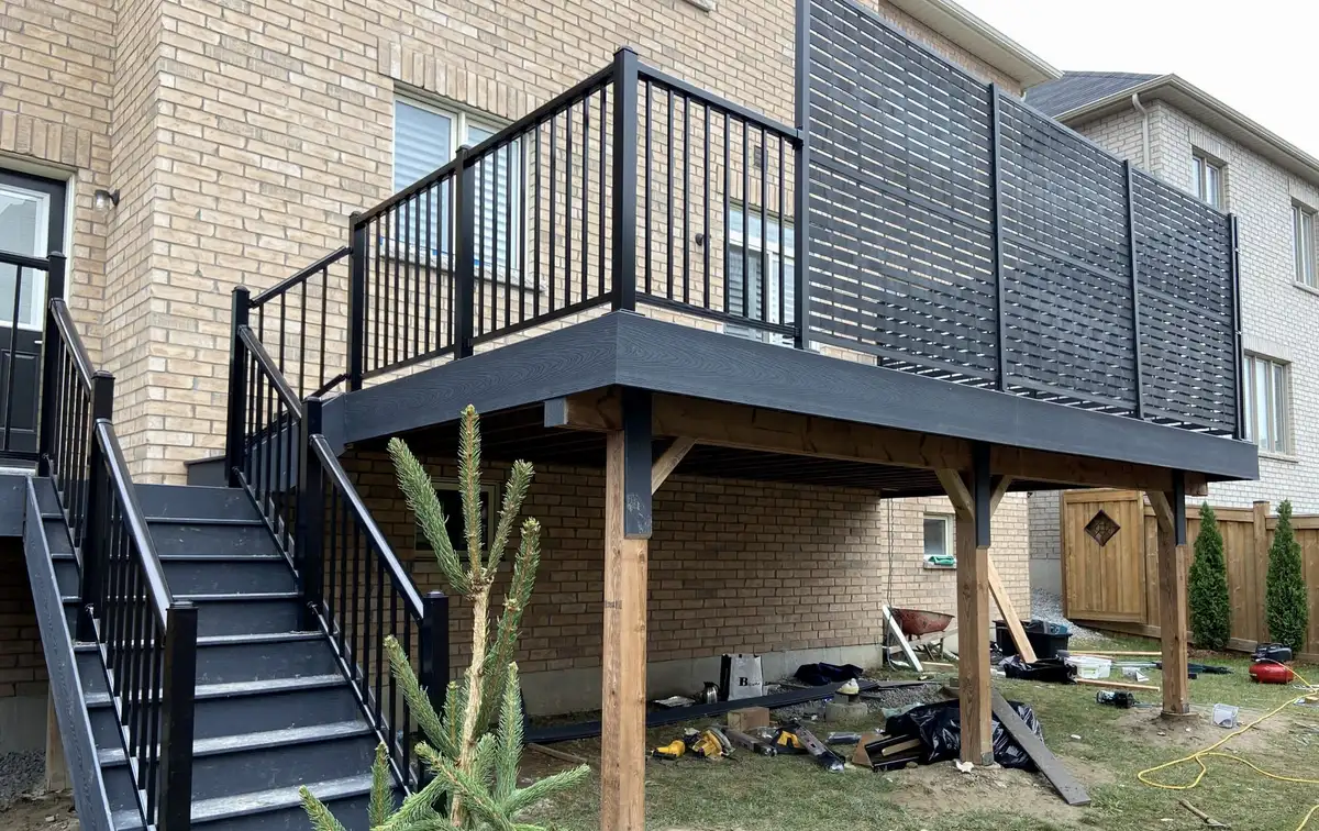 A raised charcoal composite deck with black aluminum railings, a black slatted privacy screen on one side and stairs down to the yard.