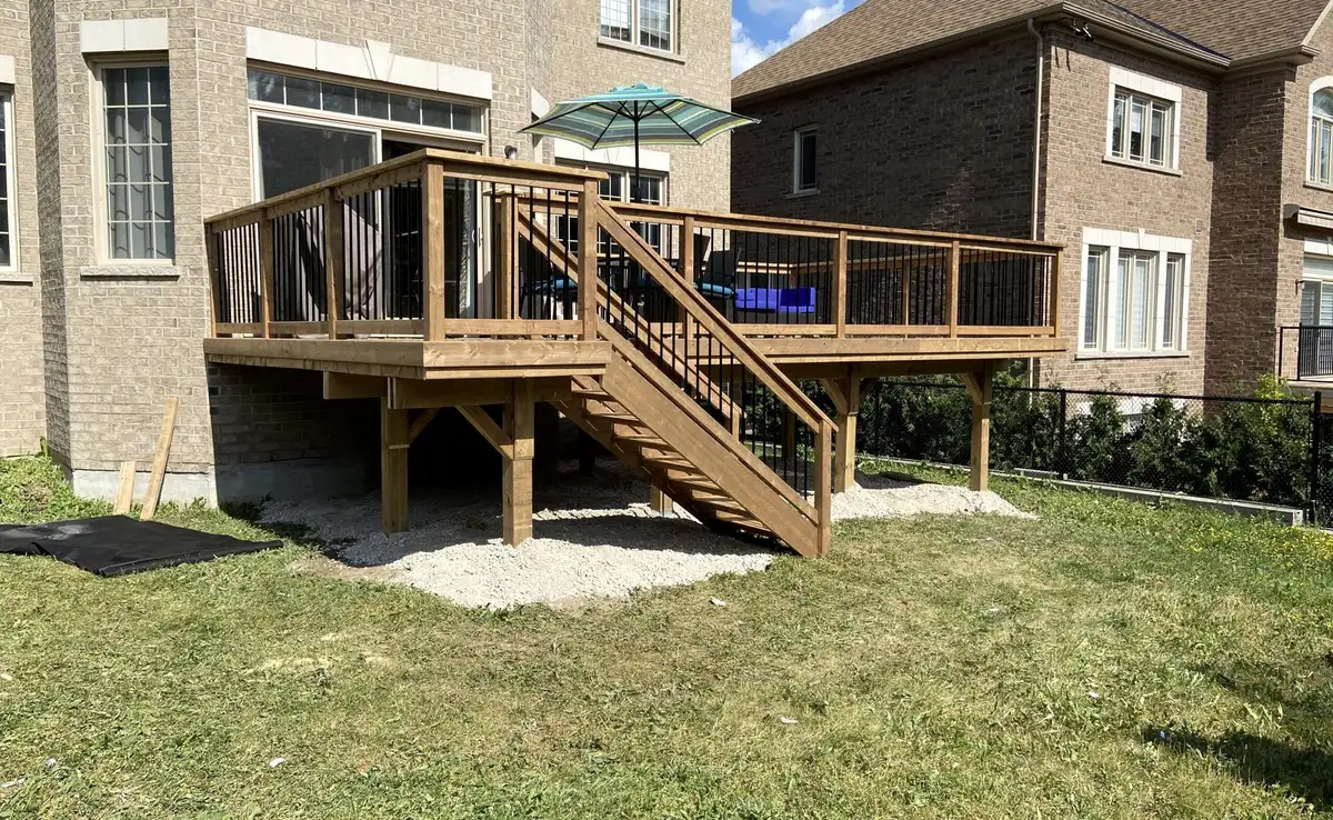 A raised pressure-treated wood deck with black balusters and a stair down to the lawn, across the back of a large brick house.