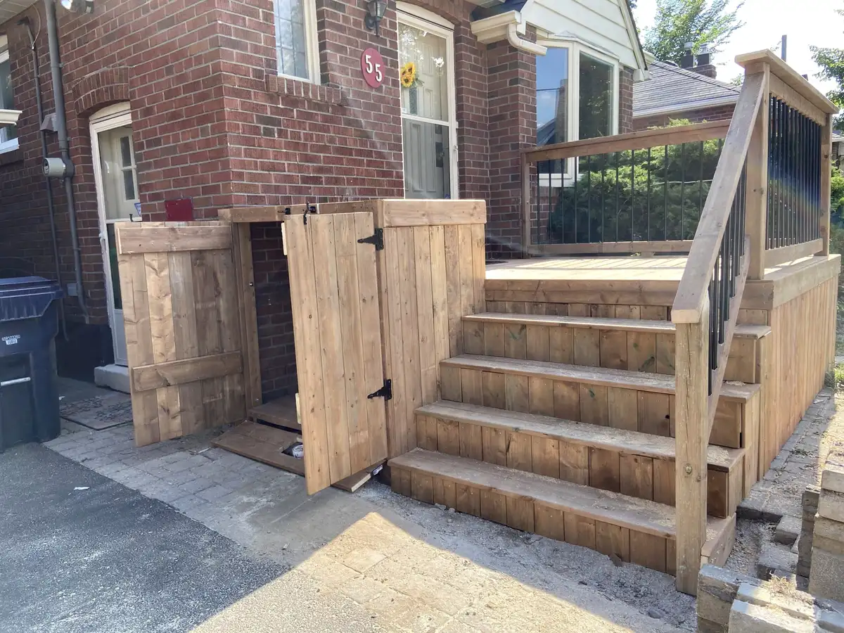 Pressure-treated wood steps rising to a side door, beside a new wood gate and fence panel.