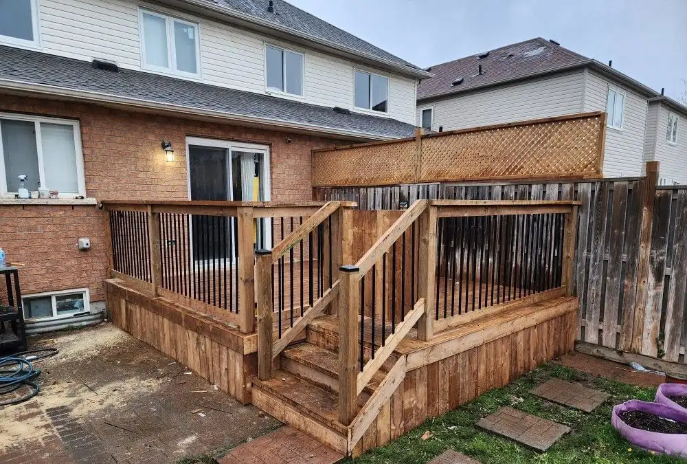 A two-level pressure-treated wood deck with black balusters and steps, backed by a lattice privacy screen, behind a brick and siding house.