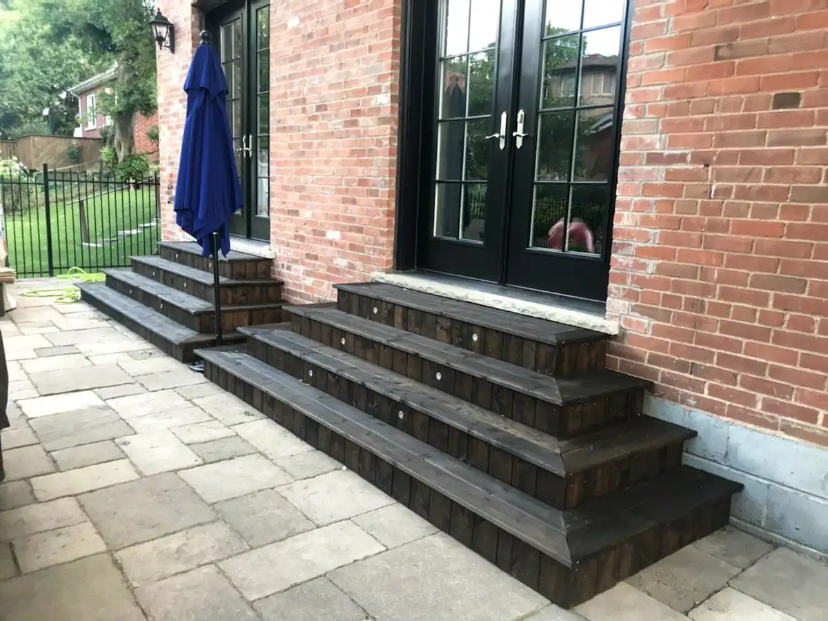 Broad charcoal composite steps leading down from a pair of French doors in a red-brick wall to a flagstone patio.