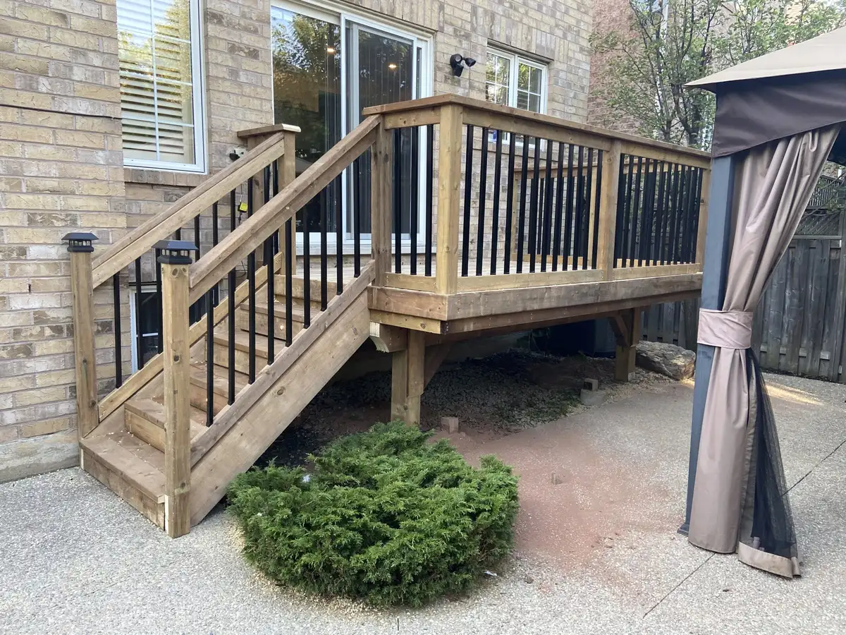A pressure-treated wood deck with black balusters and a stair down to a gravel yard, next to a fabric gazebo.