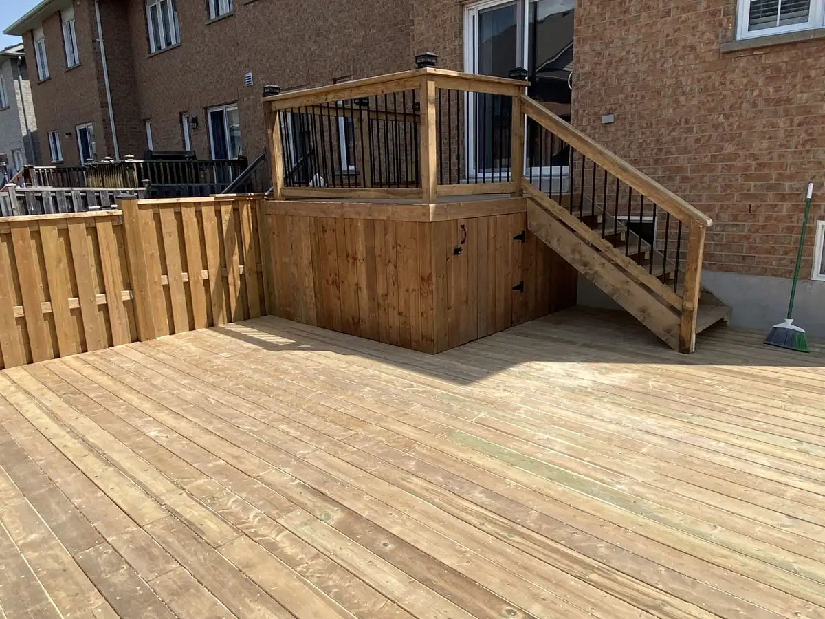 A large, low pressure-treated deck filling a backyard, with an upper landing and stair against the brick house and a wood privacy fence around it.